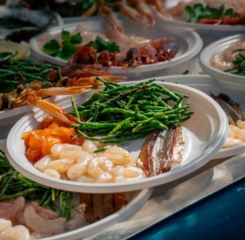 Fresh seafood selection at Catania’s fish market, featuring marinated raw fish, shrimp, anchovies, and sea asparagus served on plates. Authentic street food experience in Sicily.